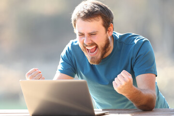 Excited man checking laptop content outdoors
