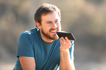 Happy man using voice recognition on cellphone outdoors
