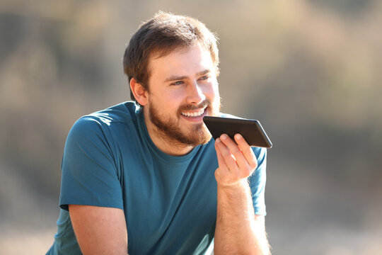 Happy man using voice recognition on cellphone outdoors