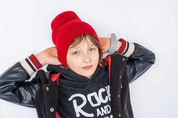 Portrait of calm pre-adolescent boy with a nose piercing, in fashionable clothes and lying on a white background and looking at camera. Adolescence and transition age. Advertising of teenage clothes.