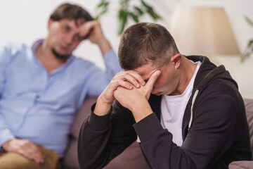 frustrated, young man is sitting at home on couch. difficult teenager covers his face with his...