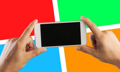 A smartphone with blank screen in hand against the background of Microsoft logo.