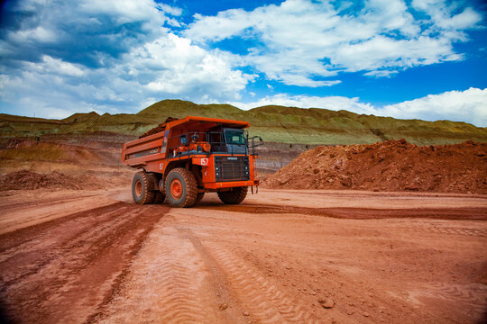 Arkalyk, Kazakhstan - May 15 2012: Orange Hitachi dump-truck with bauxite clay. Aluminium ore mining and transporting. Open-pit mine (quarry). Blue sky, white clouds.