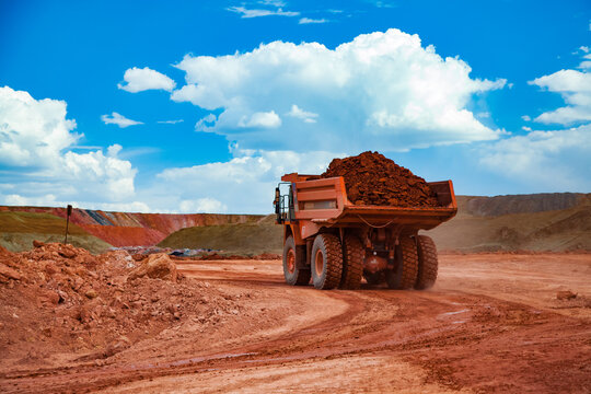 Arkalyk, Kazakhstan - May 15 2012: Mining and transporting aluminium ore. Quarry (Open-cut) mining. Orange Hitachi quarry dump-truck carrying bauxite clay. On blue sky with white clouds.