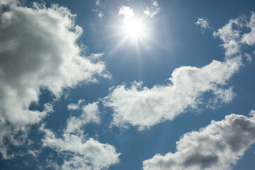 Sunbeams of a bright sun on a summer day. Shining sun through blue sky with clouds.