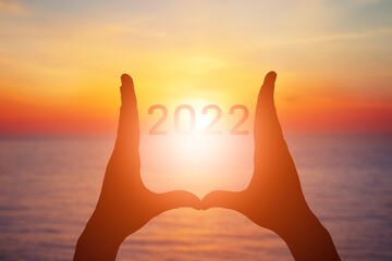 2022 is supported by hands on the background of a sunny sunset.