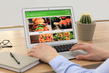 Man using laptop for ordering food online at table indoors, closeup. Concept of delivery service