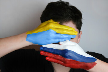 Hand painted in the colors of the flag of Russia and Ukraine. War in Ukraine. Concept of war between Ukraine and Russia. The palms cover the young man's face. 