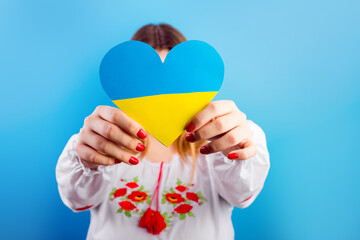 A young Ukrainian girl in an embroidered shirt holds a heart of a yellow-blue flag. The concept of...