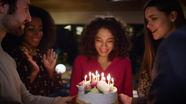 Friends surprising birthday girl with burning candles cake at celebration party.