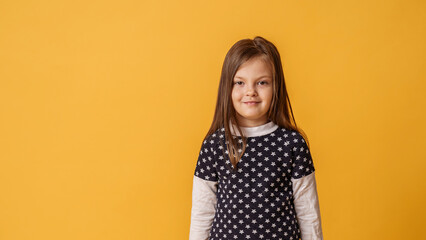 Obraz premium Portrait of a charming little girl, smiling sweetly standing on a yellow background in the studio. The child is positive and looks at the camera with confidence. Advertising
