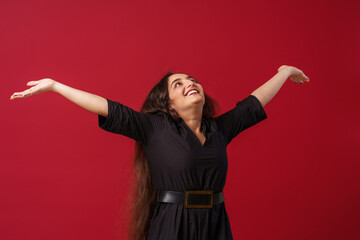 Portrait of a happy girl with dark long hair, smiling. A young woman, emotionally excited, looks into the camera, standing on a red background in the studio
