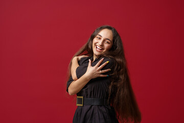 Portrait of a happy girl with dark long hair, smiling. A young woman, emotionally excited, looks into the camera, standing on a red background in the studio