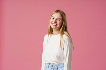 Obraz premium Portrait of a happy girl with long blonde hair, smiling and rejoicing. A teenager, emotionally excited with delight, looks into the camera, standing on a pink background in the studio
