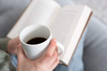Closeup of hand holding cup of coffee with a book on background
