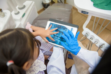 Female dentist explaining teeth x-ray to a little girl in dental clinic, teeth check-up and Healthy...