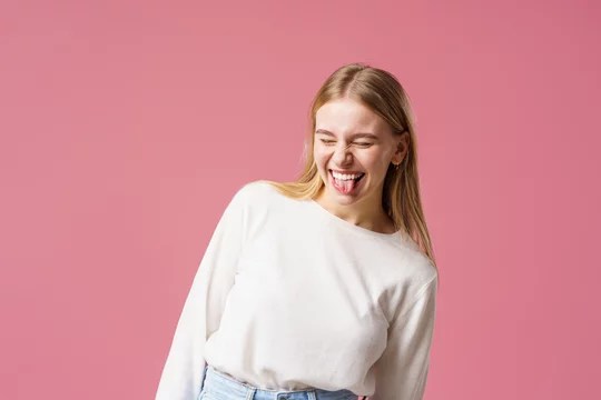 Portrait of a happy girl with long blonde hair, smiling and rejoicing. A teenager, emotionally excited with delight, closes his eyes, standing on a pink background in the studio foto de Stock |