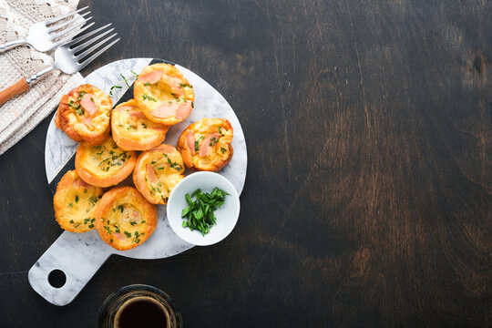 Delicious egg muffins with green onions, bacon, cheese and tomatoes on wooden board on old wooden rustic background. Healthy high protein and low carb breakfast. Homemade food.