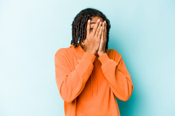 Young African American man isolated on blue background blink through fingers frightened and nervous.