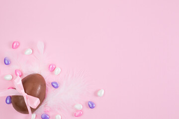 Colorful Easter chocolate eggs, purple bows, flat lay on pink background. Happy Easter. Stylish Easter layout. Greeting card or banner template