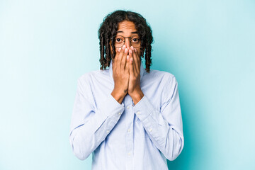 Young African American man isolated on blue background shocked, covering mouth with hands, anxious to discover something new.