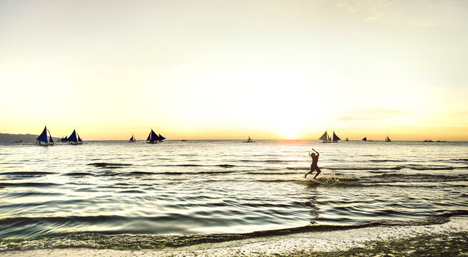 Silhouette of skimboarder at sunset with typical sailing boats at Boracay island - Extreme sport and exclusive travel concept in Philippines - Warm sunshine filtered look