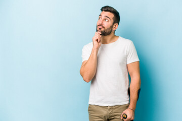 Young man with crutches isolated on blue background looking sideways with doubtful and skeptical...