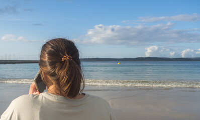 Back view of a woman talking on a smartphone on a beach at sunset.
