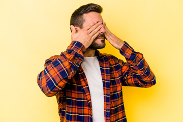 Young caucasian man isolated on yellow background afraid covering eyes with hands.