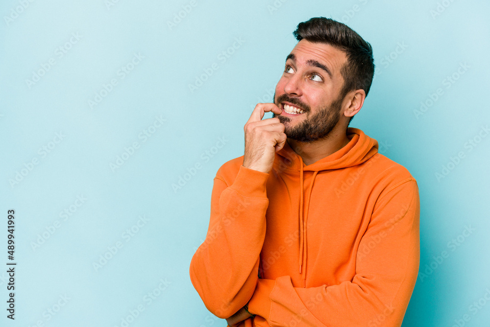 Wall mural Young caucasian man isolated on blue background relaxed thinking about something looking at a copy space.