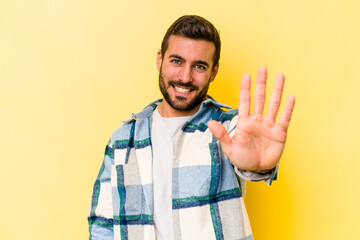 Young caucasian man isolated on yellow background smiling cheerful showing number five with fingers.