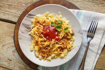 Bolognese pasta garnished with herbs and cheese in a plate on a round stand next to a fork and a napkin.