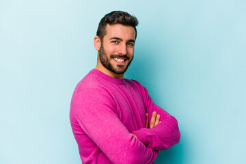 Young caucasian man isolated on blue background who feels confident, crossing arms with determination.