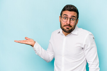 Young caucasian man isolated on blue background showing a copy space on a palm and holding another...