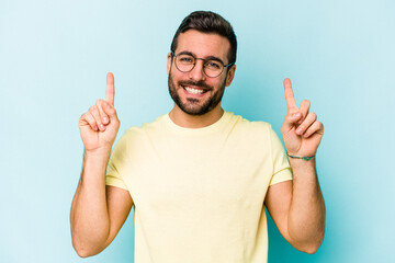 Young caucasian man isolated on blue background indicates with both fore fingers up showing a blank space.