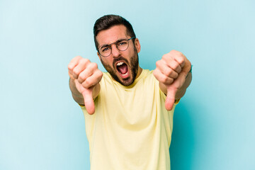 Young caucasian man isolated on blue background showing thumb down and expressing dislike.