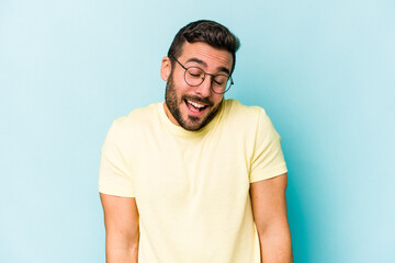 Young caucasian man isolated on blue background laughs and closes eyes, feels relaxed and happy.