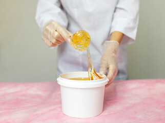 The master of sugar hair removal winds the epilation paste onto the spatula. Wax epilation spa procedure. Liquid yellow sugar paste or wax for depilation on a wooden stick on a white background
