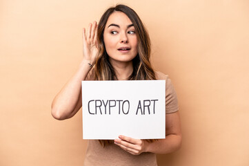 Young caucasian woman holding a crypto art placard isolated on beige background trying to listening a gossip.