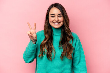 Young caucasian woman isolated on pink background joyful and carefree showing a peace symbol with...