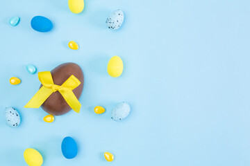 Broken and whole chocolate Easter eggs, multicolored sweets on blue background. Concept of celebrating Easter, Easter decorations, search for sweets for Easter Bunny. Flat lay, top view. Copy Space.