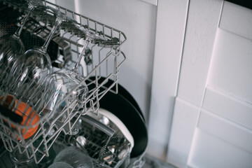 Open dishwasher with clean dishes in a white kitchen. Clean glasses, plates, mugs in the dishwasher...