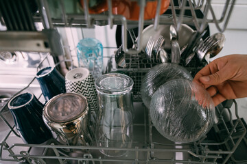 Weekend homework. Close-up of male hands removing clean glass and ceramic dishes from an open dishwasher.