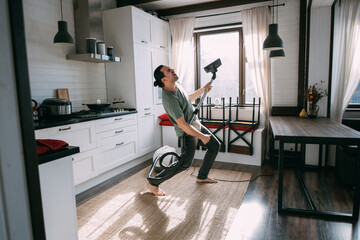 Young happy man doing cleaning and dancing with vacuum cleaner in kitchen and living room at home.