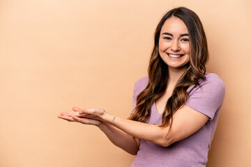 Young caucasian woman isolated on beige background holding a copy space on a palm.