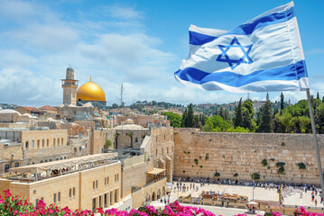 Fototapeta premium An Israeli flag blows in the wind as jewish orthodox believers read the Torah and pray facing the Western Wall, also known as Wailing Wall in Old City in Jerusalem, Israel. 