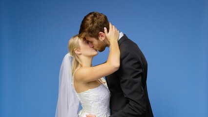 The bride and groom in wedding suits kiss on a blue background. Wedding