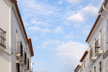 Fototapeta na wymiar Artistic image of two building facades with white walls and a beautiful blue sky with clouds in the background conveying tranquillity. Top floors of two small buildings in a village on a sunny day.