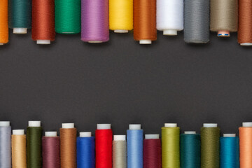 Colored sewing threads are laid out on a gray background, space for text.