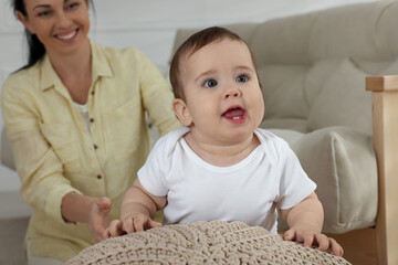 Happy mother with her cute baby near sofa at home